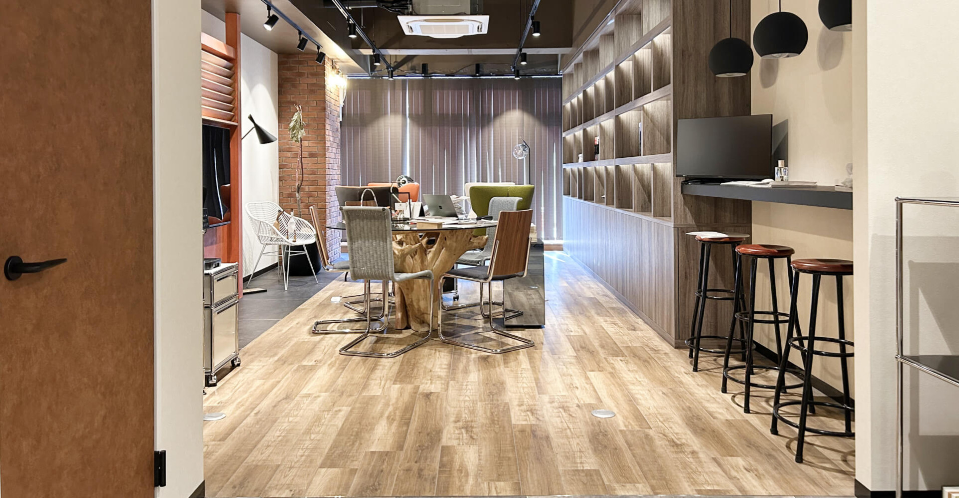 木目調の床と大きな書棚、多様な椅子が並ぶオフィス