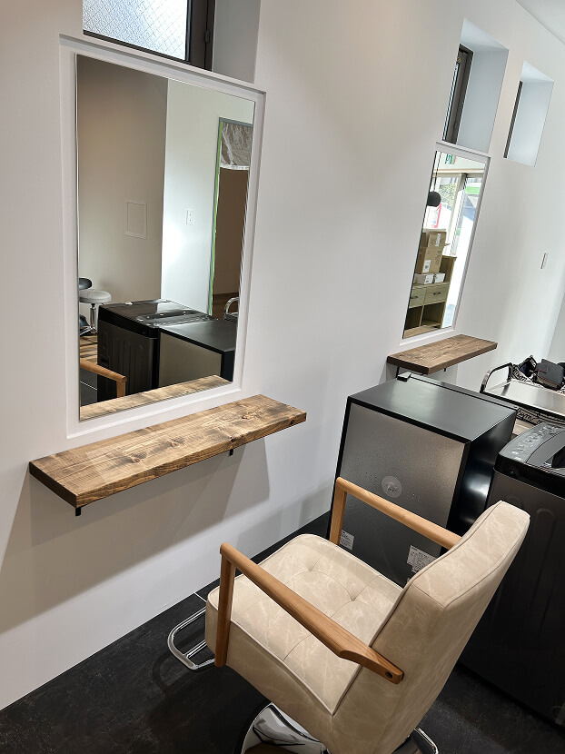 大きな鏡と木製棚、ベージュの椅子を配した施術スペース。