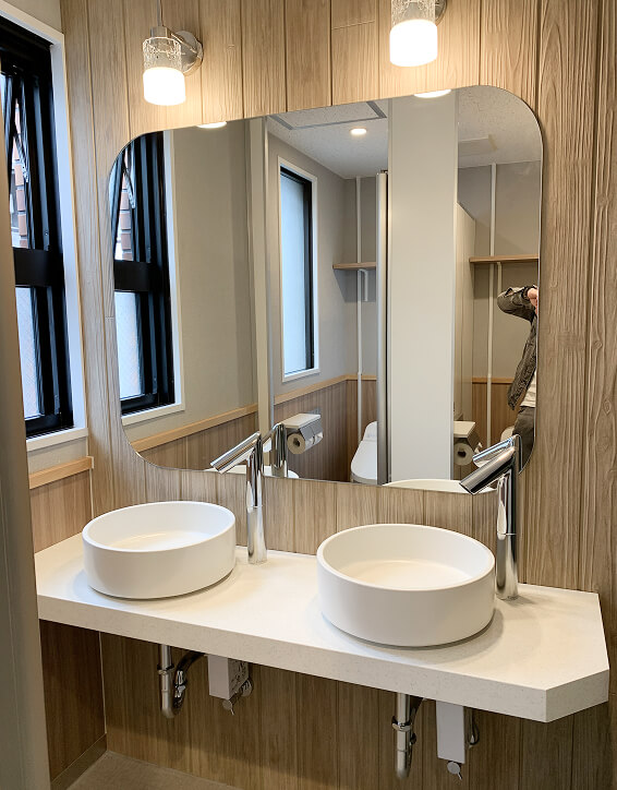 木目調の壁に丸い洗面ボウルが2つ並んだ清潔感のある洗面所