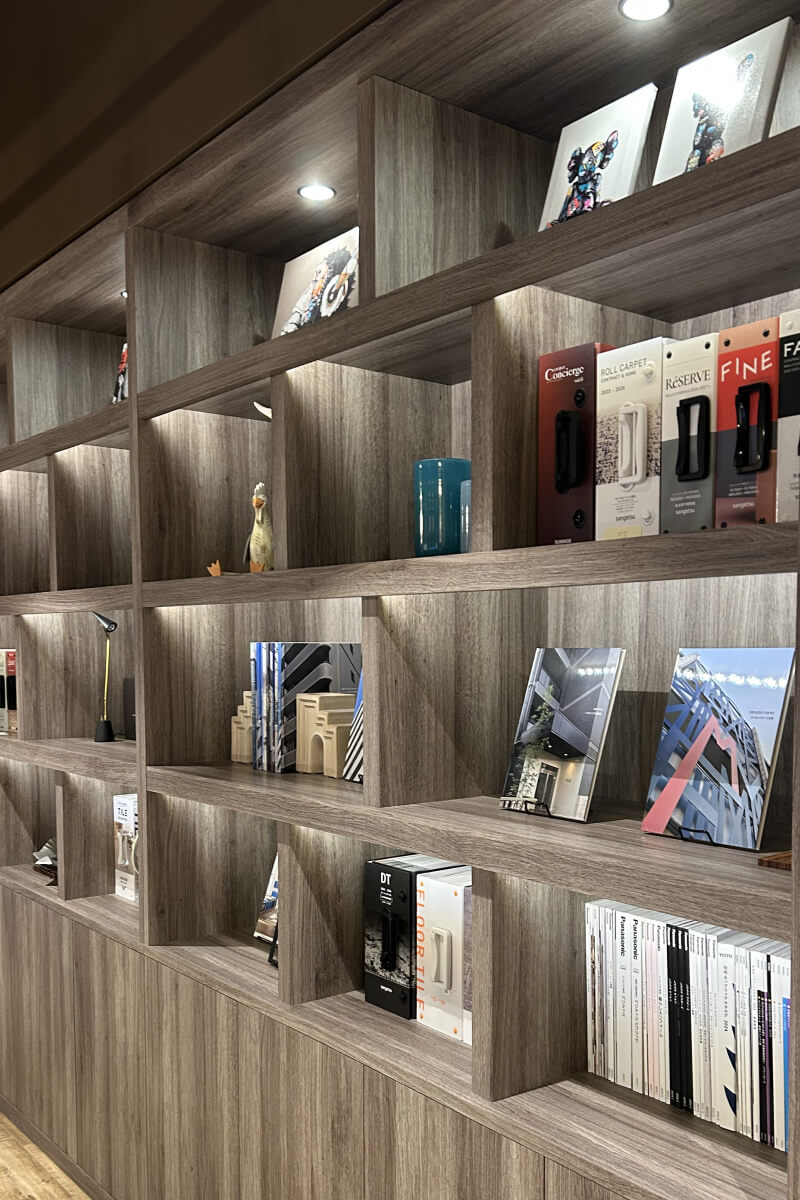 カタログや小物が整然と並ぶ、照明付きの大きな木製壁面収納。