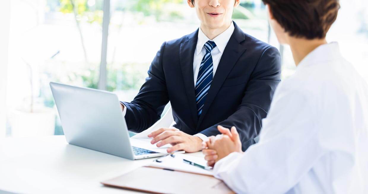 ビジネスの打ち合わせ： 明るいオフィスで、PCを前に資料を見ながら相談するビジネスマン