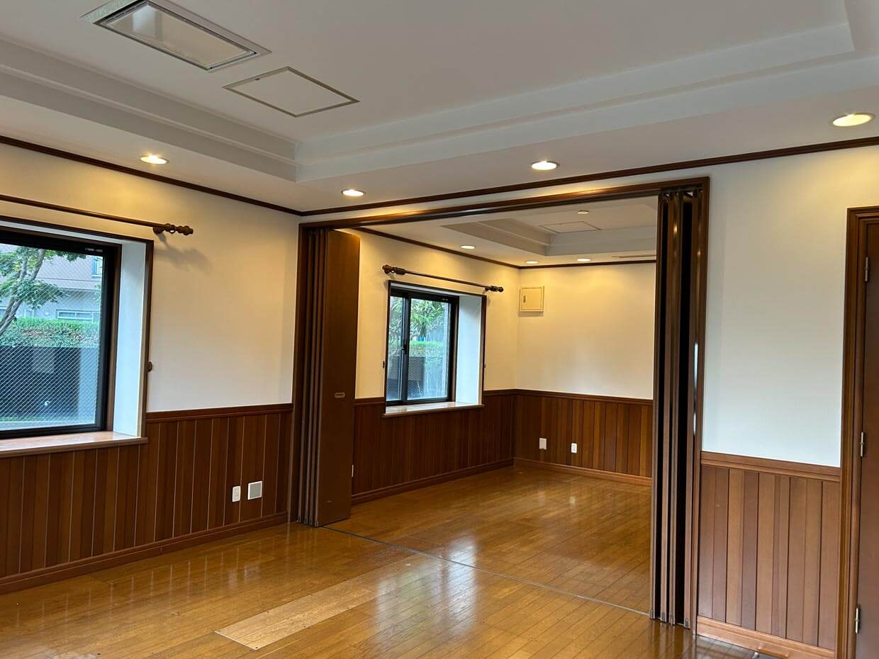 リフォーム後の室内： 木目調の腰壁と折りたたみ戸で仕切られた、落ち着いた印象の部屋。