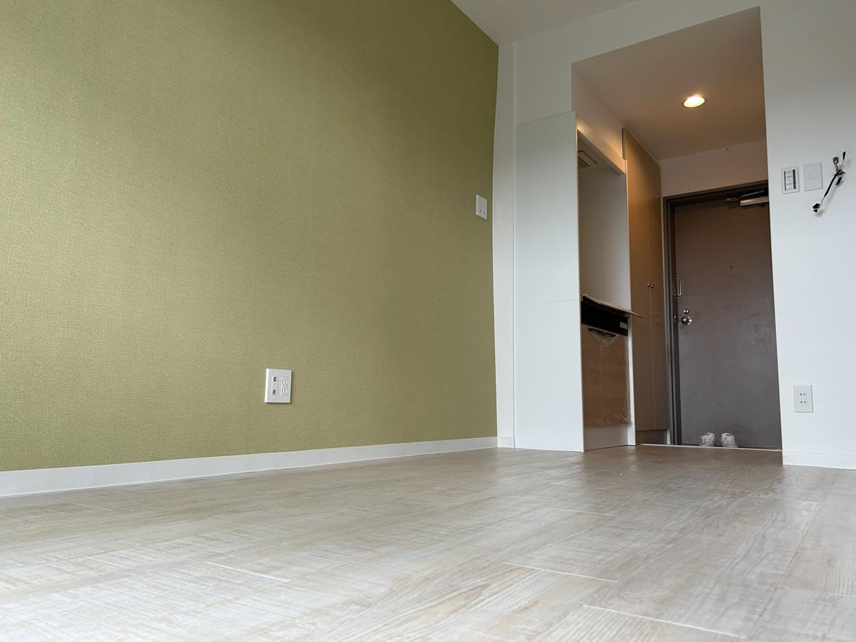 グリーンのアクセント壁： 柔らかなグリーンの壁紙と明るい床材を合わせた清潔感のある室内。