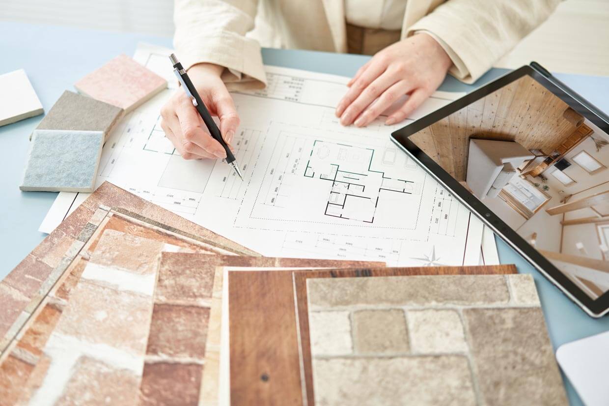 素材と図面： サンプル資料やタブレットを並べ、図面を前に打ち合わせる様子。